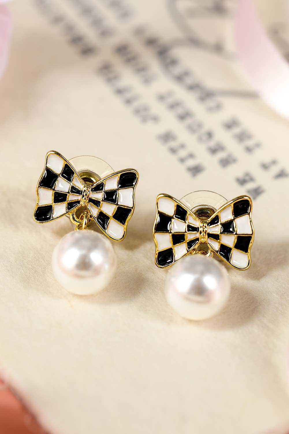 Bow-shaped earrings with pearl-like centers on a textured surface