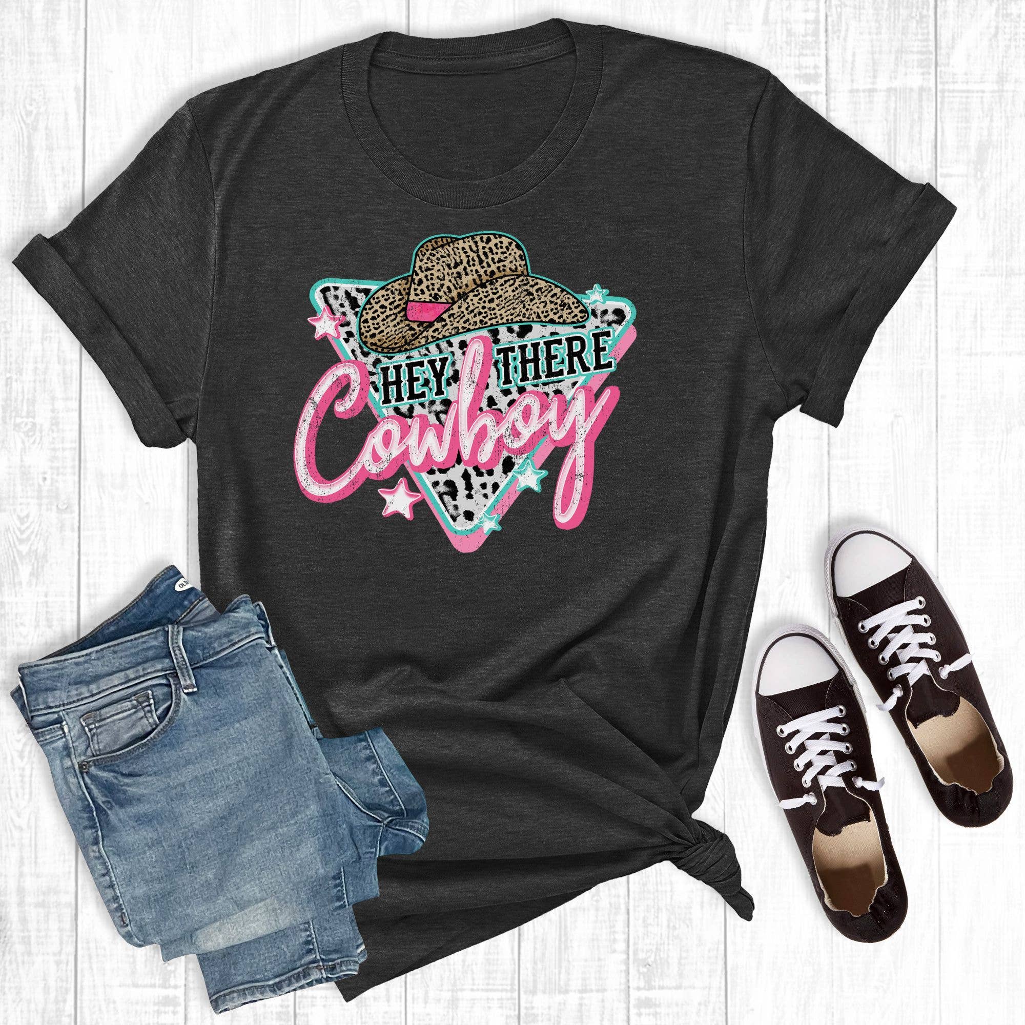 Black t-shirt with 'Hey There Cowboy' graphic, paired with denim shorts and black sneakers on a light wooden floor.