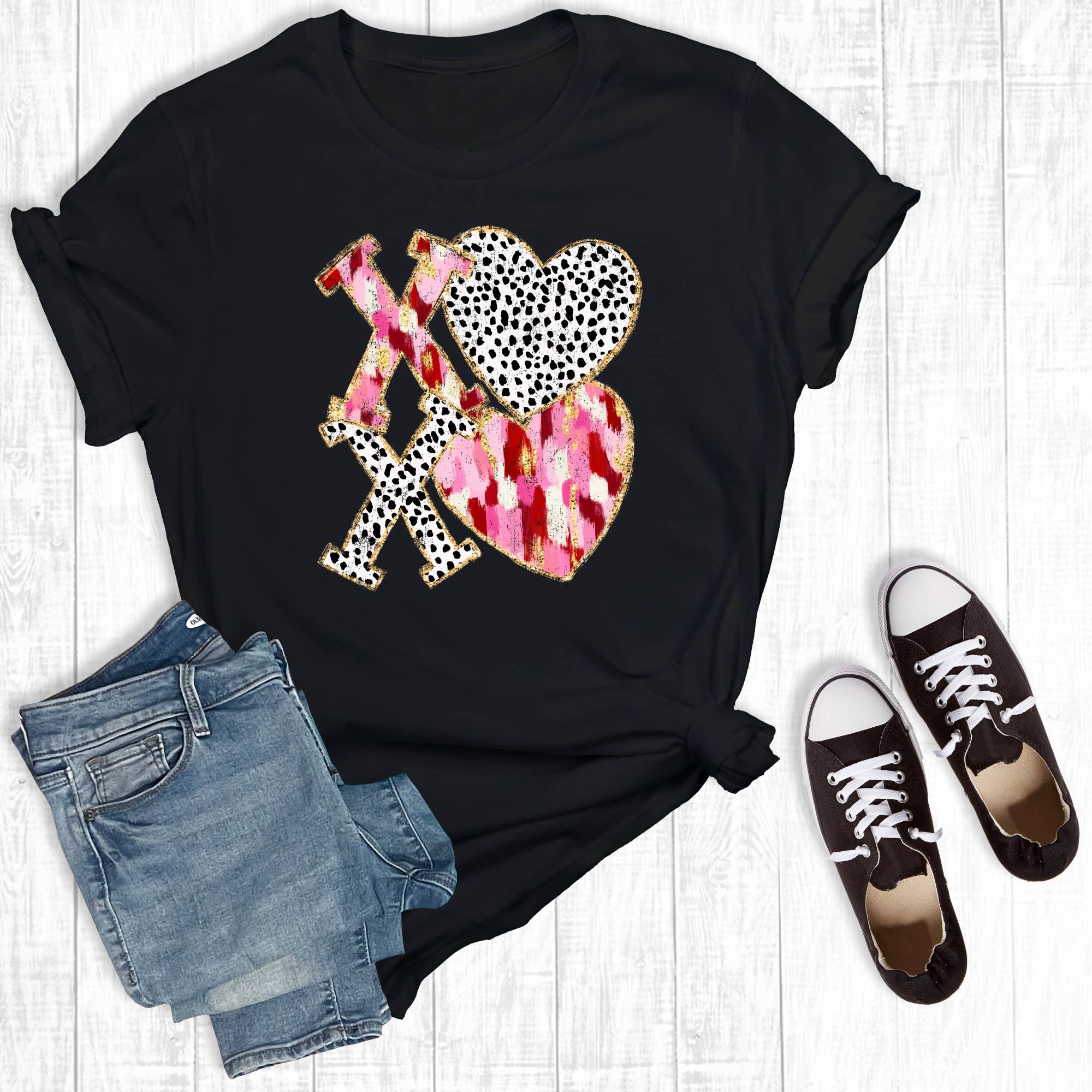 Black t-shirt with colorful graphic design, paired with denim shorts and black sneakers on a light wooden surface.