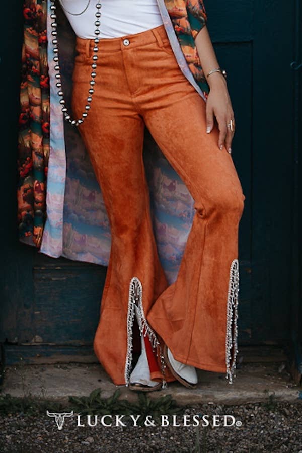 Person wearing orange flared pants with fringe details, standing against a dark background.