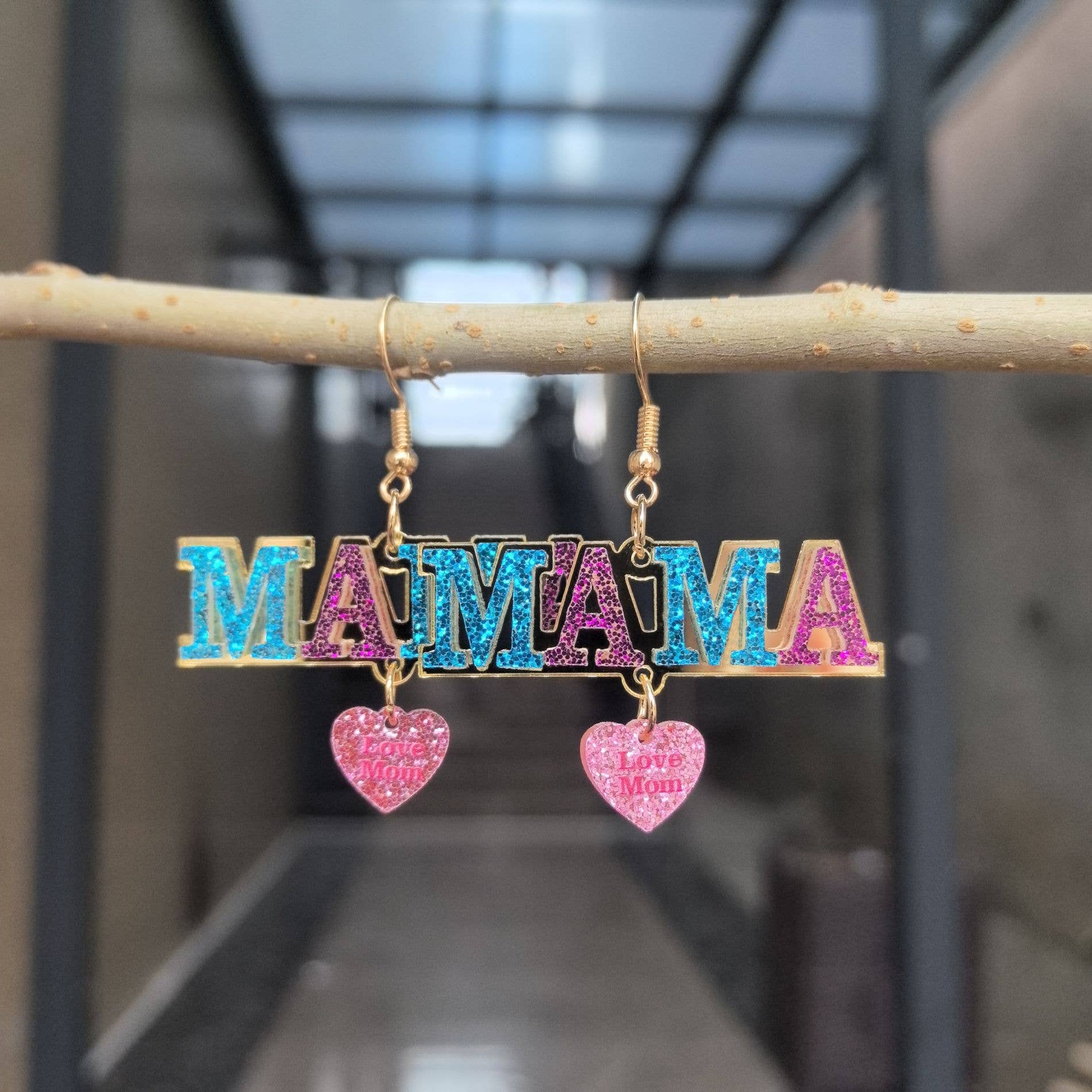 Colorful 'MAMA' earrings with heart charms hanging on a branch.