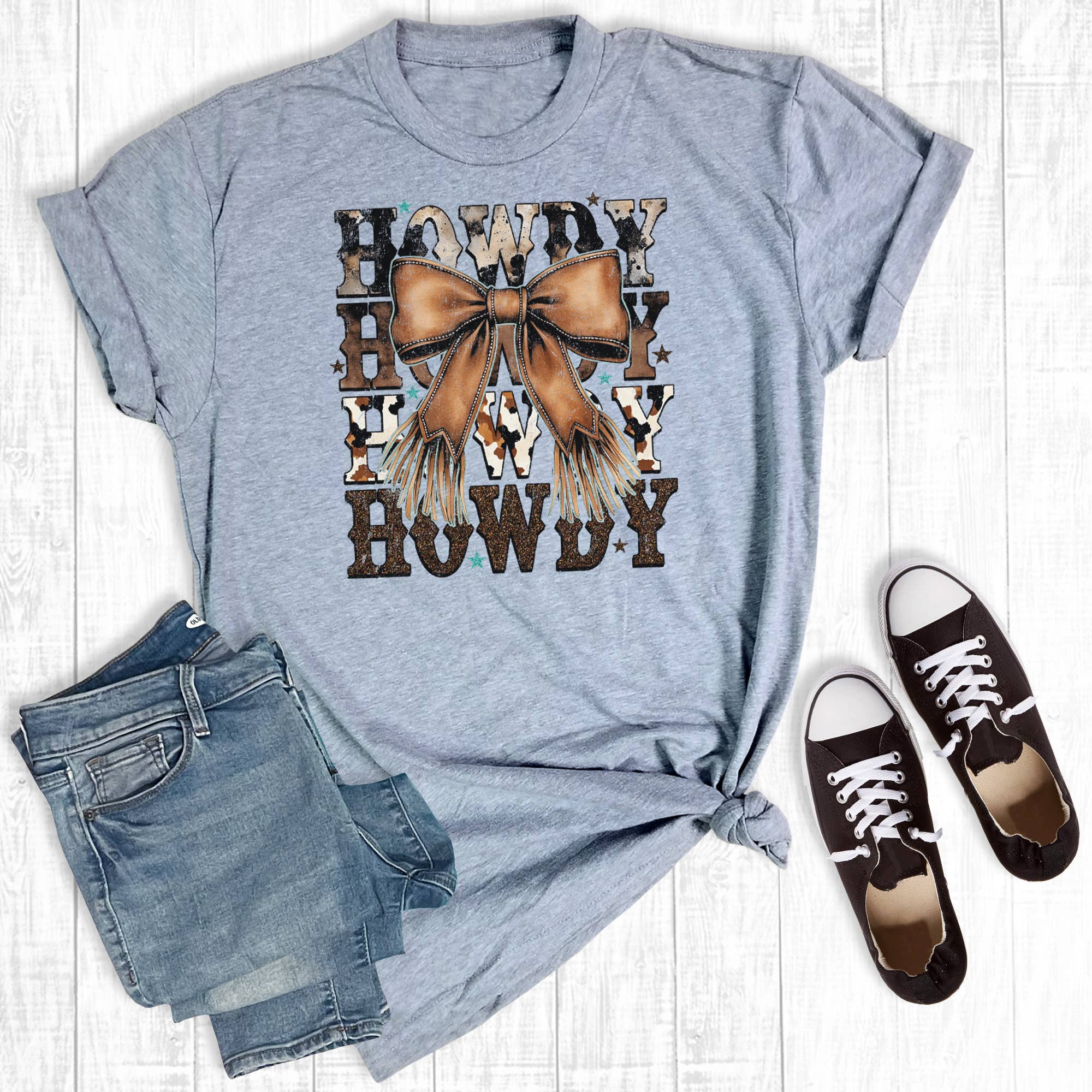Gray t-shirt with 'Howdy' graphic, denim shorts, and brown sneakers on a wooden surface