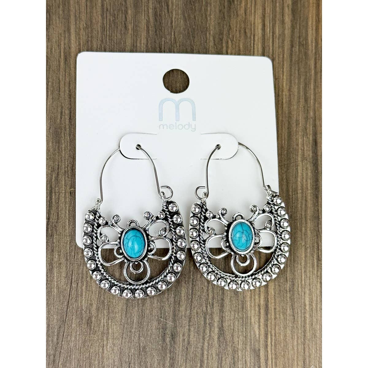 Pair of silver hoop earrings with turquoise stones on a Melody brand card, against a wooden surface.