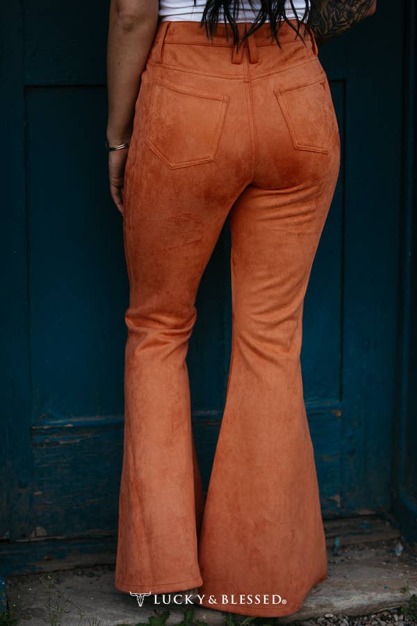 Person wearing orange flared pants standing against a blue wall with 'Lucky & Blessed' branding.