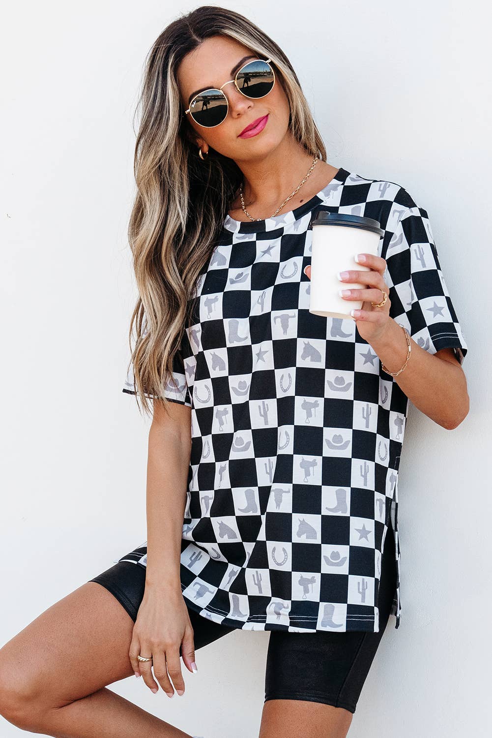 Woman wearing a black and white checkered dress holding a cup against a white background