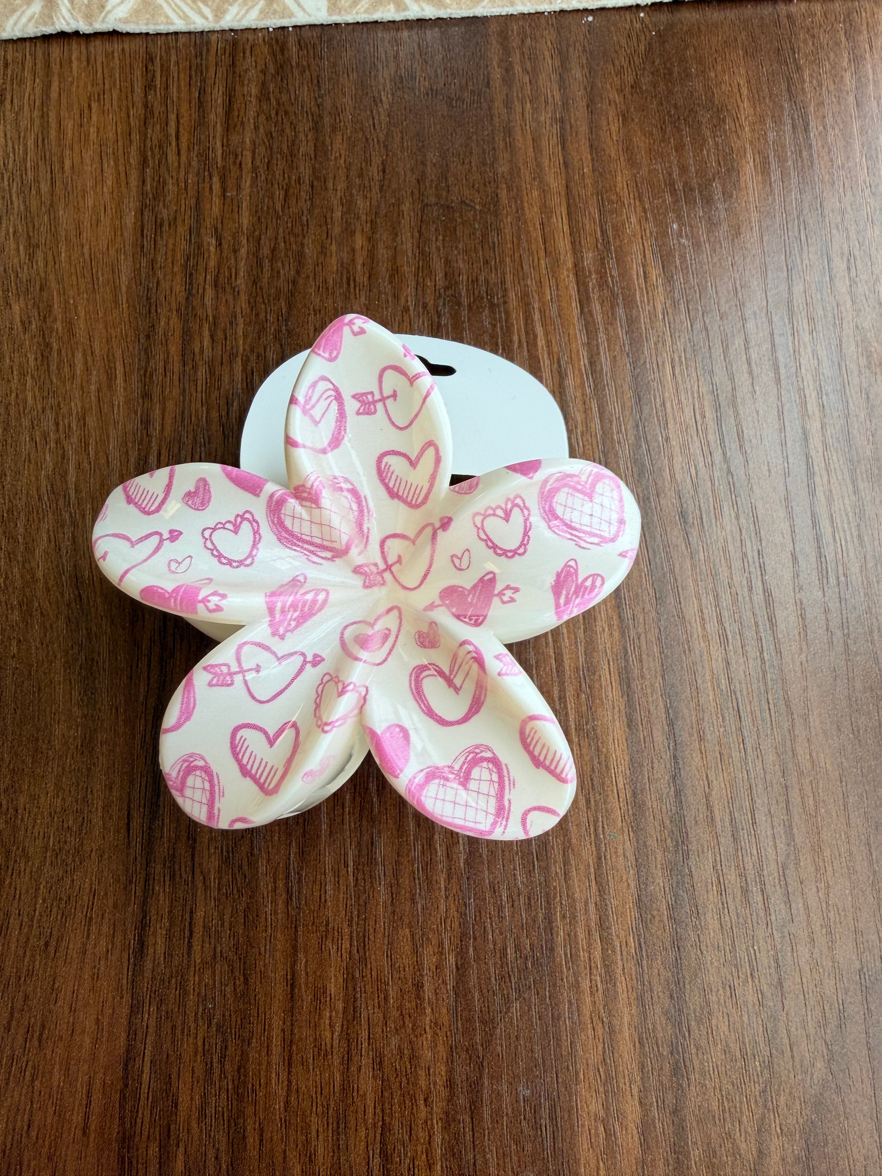 Flower-shaped hair clip with pink heart pattern on a wooden surface