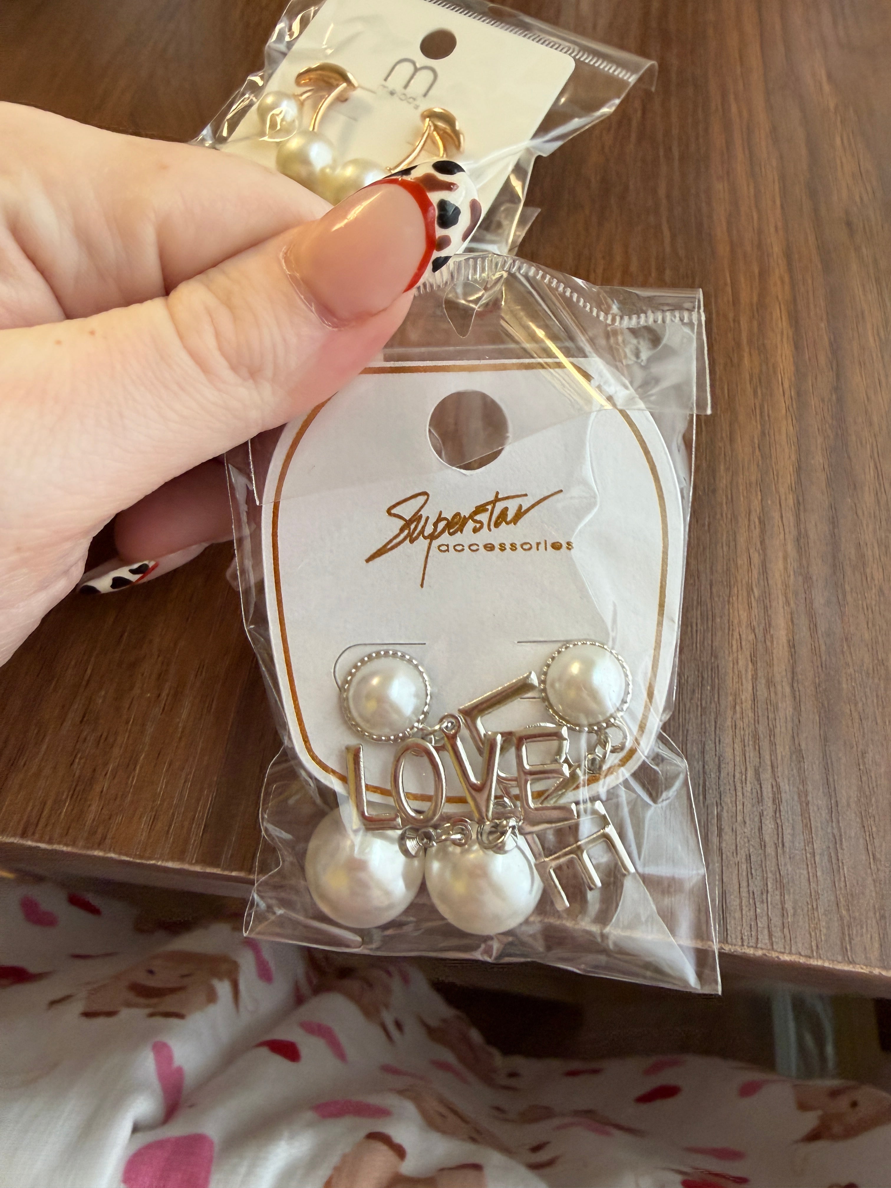 Packaged earrings with 'LOVE' text held by a hand on a wooden surface