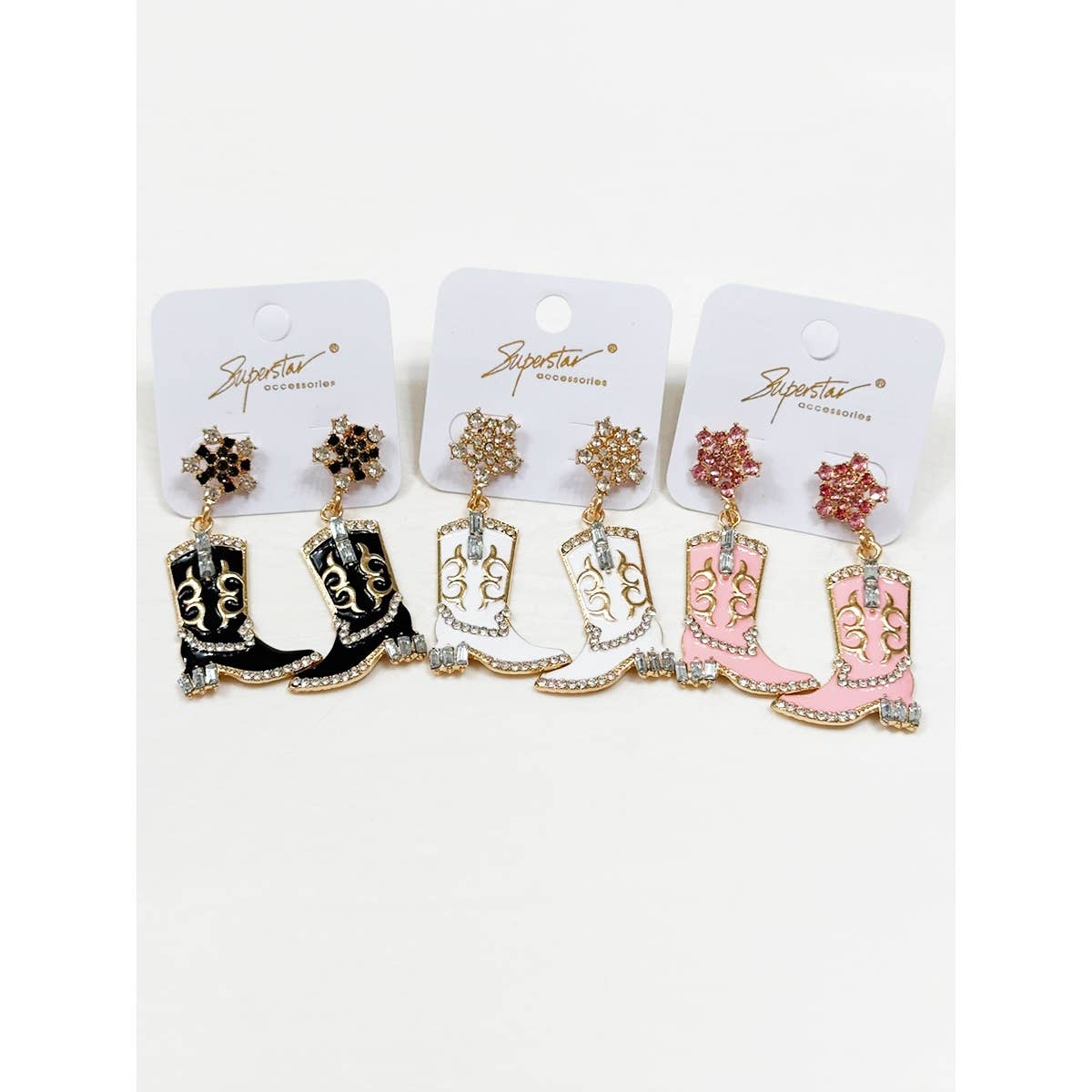 Three pairs of cowboy boot earrings on branded cards against a white background