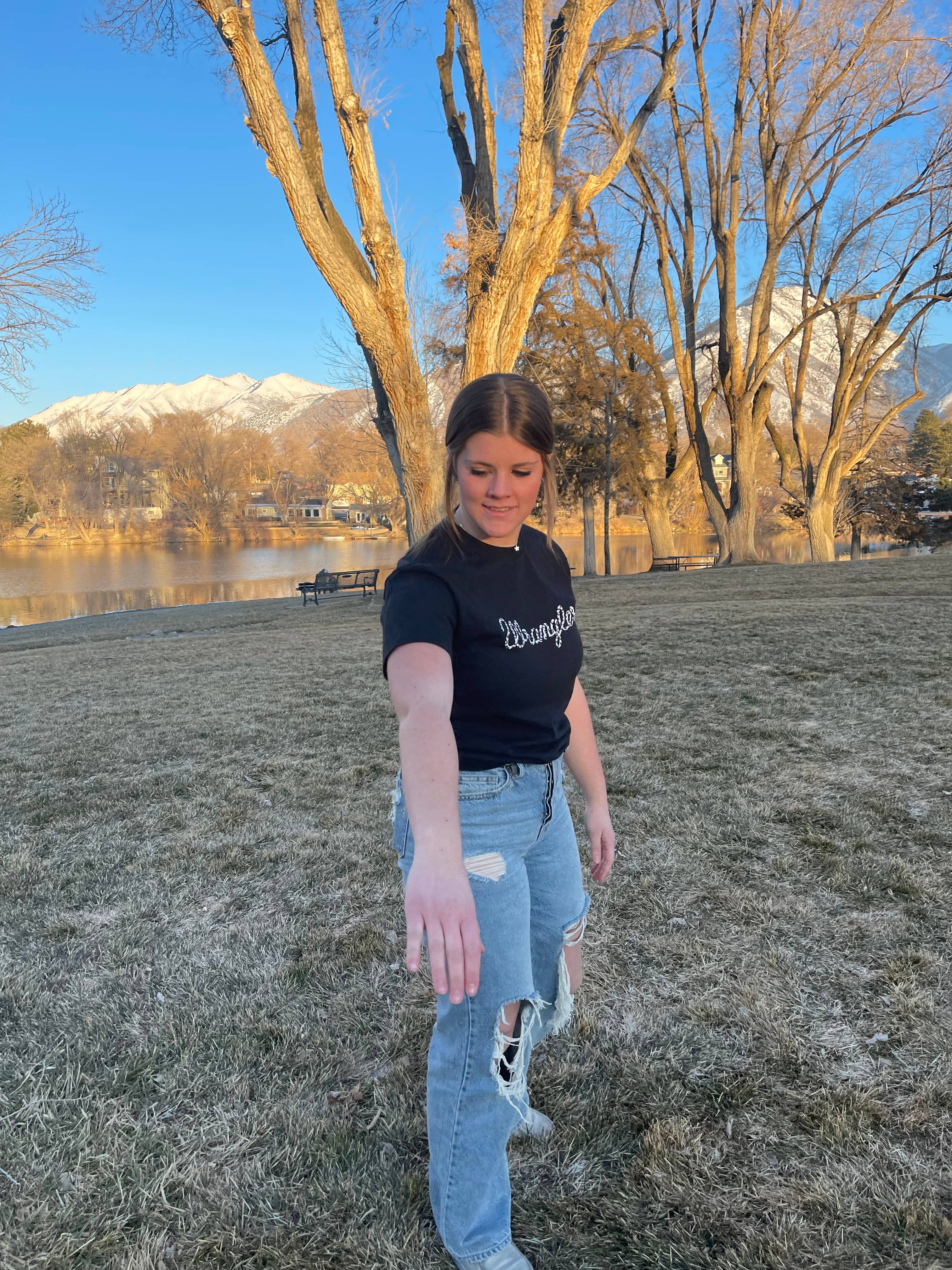 Person standing in a park with trees and mountains in the background
