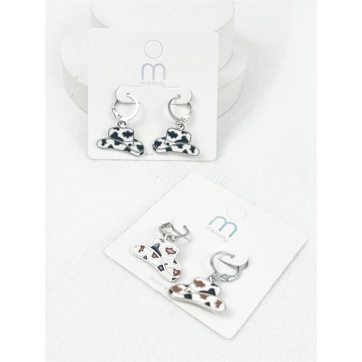 Pair of earrings with cowgirl hat and saddle design on a branded card.