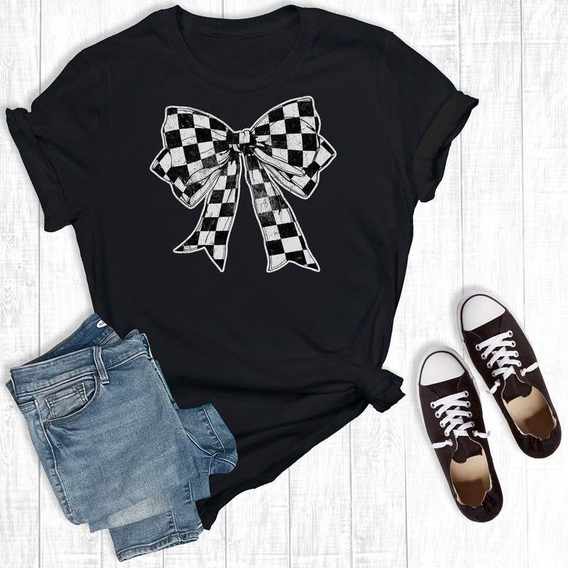 Black t-shirt with a checkered bow design, paired with denim shorts and brown sneakers on a light wooden surface.