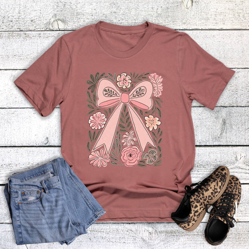 Mauve t-shirt with a pink bow and floral design, paired with denim shorts and leopard print shoes on a wooden surface.
